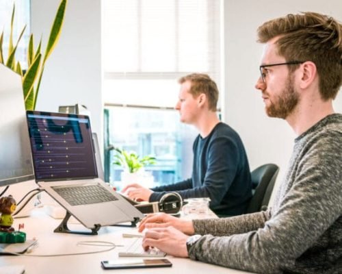 Dois homens trabalhando em notebooks ligados a monitores