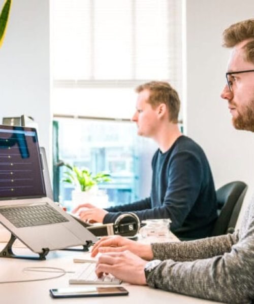 Dois homens trabalhando em notebooks ligados a monitores