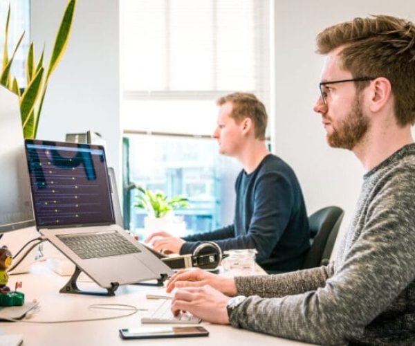 Dois homens trabalhando em notebooks ligados a monitores